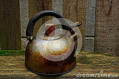 Old rusty and dirty teapot is standing by the wooden fence Stock Photo