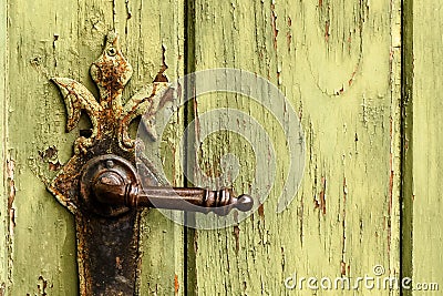 Old rusty door handle on green door. Detail of rustic old vintage and rusty grungy iron door handle installed on an ornamented old Stock Photo