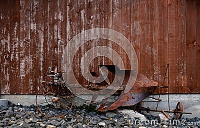 An old and rusty horse plow in front of a weathered wooden barn wall Stock Photo