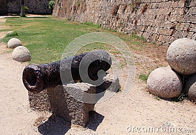 Old rusty medieval cannon in the drained moat surrounding the walls of Rhodes Fortress and Rhodes Old Town Stock Photo