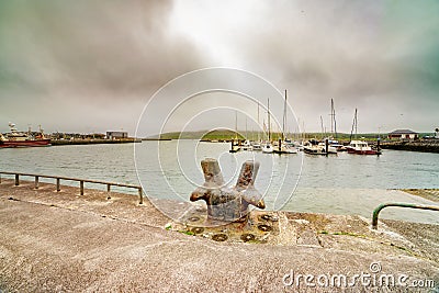 Old rusty metal bollard and ships in the Dingle harbour at hazy day Stock Photo