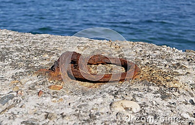 An old rusty metal mooring ring on the mooring wall on a sunny summer day. A device for holding sea vessels in port. Stock Photo