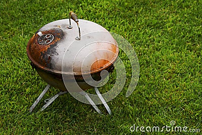 Old rusty small barbeque cooker in a garden. Cheap metal cooking device. Worn out budget way to cook food Stock Photo