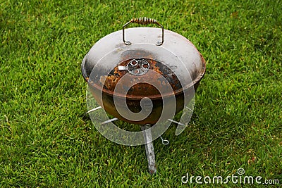 Old rusty small barbeque cooker in a garden. Cheap metal cooking device. Worn out budget way to cook food Stock Photo
