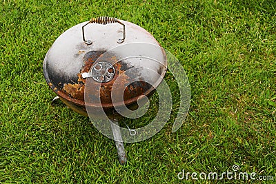 Old rusty small barbeque cooker in a garden. Cheap metal cooking device. Worn out budget way to cook food Stock Photo