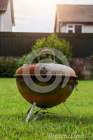 Old rusty small barbeque cooker in a garden. Cheap metal cooking device. Worn out budget way to cook food Stock Photo