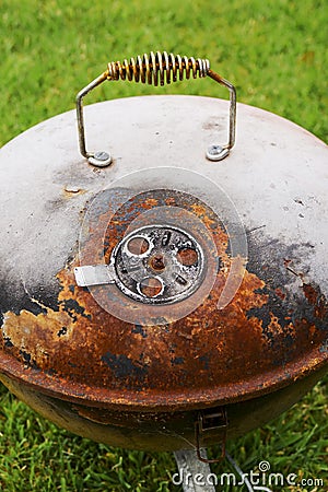 Old rusty small barbeque cooker in a garden. Cheap metal cooking device. Worn out budget way to cook food Stock Photo