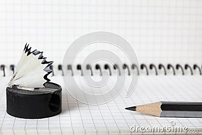 An old, second-hand, sharpener with a shavings and a simple pencil lie on the notebook in a box. Selective focus. Close-up. Stock Photo