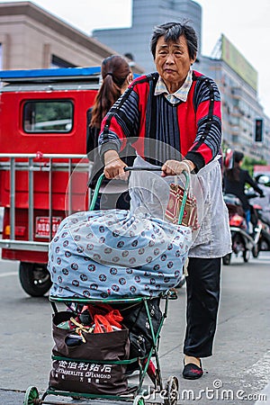 An Old senior female lady pushing cart full of belongings across busy road Editorial Stock Photo