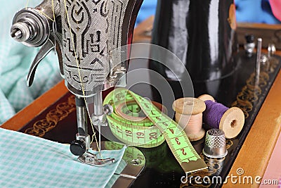 On the old sewing machine lie wooden retro coils with threads; a thimble, a measuring tape and a piece of cotton fabric. Focus on Editorial Stock Photo