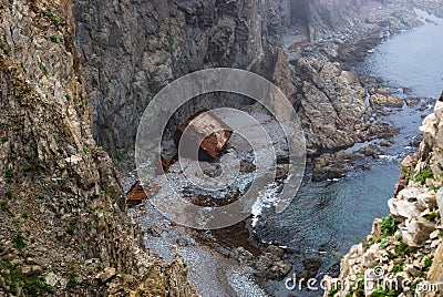An old shipwrecked ship stands on the shore at the foot of a rocky cliff. Cape Briner. Primorsky Krai. Russia Stock Photo