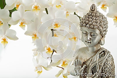 Old silver color statuette Buddha sitting in meditation pose on light blurred orchid flower background Stock Photo