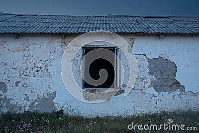 An old sinister abandoned house. The house has an empty black window. Cracked plaster Stock Photo