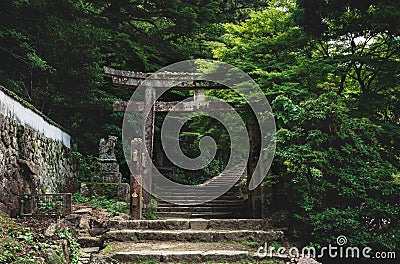 Old stone torri gate over a stairs path in park on Mount Misen in Miyajima, Hiroshima, Japan Stock Photo