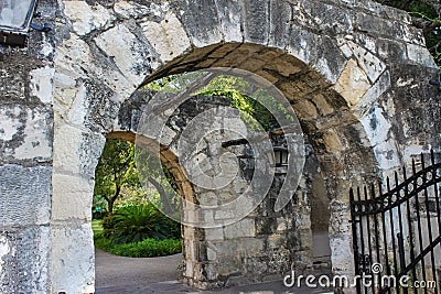 Old stone walls and archways with trees and vines and hanging lanterns and a wrong iron gate Stock Photo