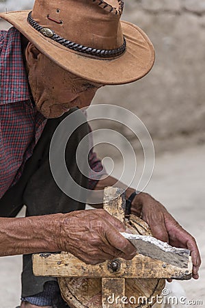 Old Tibetan man cleaning ancient wooden prayer wheel Editorial Stock Photo