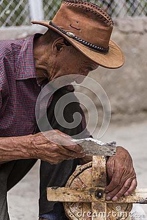 Old Tibetan man cleaning ancient wooden prayer wheel Editorial Stock Photo