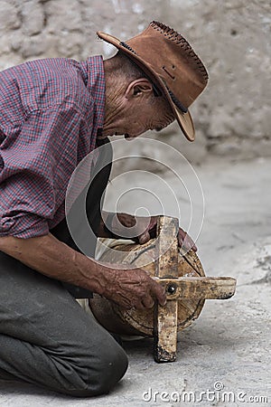 Old Tibetan man repairing ancient wooden prayer wheel Editorial Stock Photo