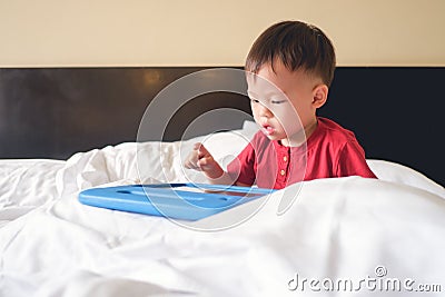 Old toddler boy child sitting in bed watching a video from tablet pc Stock Photo