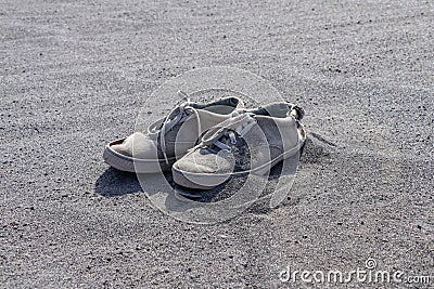 Old torn white sneakers on black volcanic sand. A pair of tie shoes with laces in volcanic ash. Discarded destroyed shoes Stock Photo