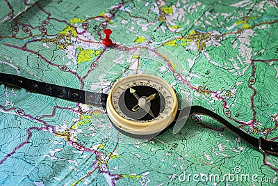 The old tourist compass on the strap is located on top of a topographic map with a red push pin. Trails and hiking trails are Stock Photo