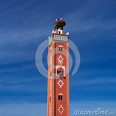 Old traditional terracotta minaret with storks nest on the top and arabic man painting ornament from the window. Morocco Stock Photo