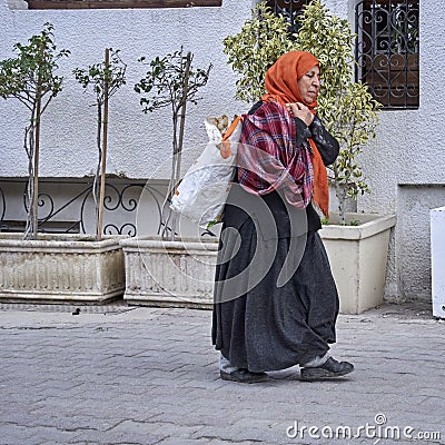Old Tunisian woman in worn clothes carries a plastic sack over her shoulder Editorial Stock Photo