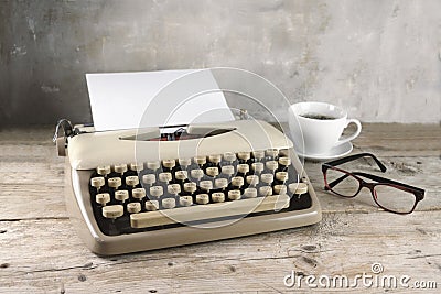 Old typewriter from the 1950s with blank paper, coffee and glasses on rustic wood, pale vintage color style, copy space Stock Photo