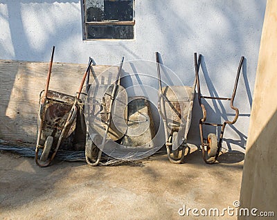 Old unused and broken wheelbarrows placed against the wall in a row outside Stock Photo