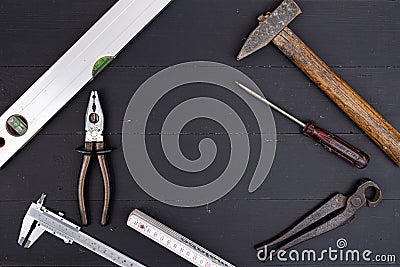 Old used hammer, pliers, libella, measuring meter, nonius and screwdriver with copy space on the black wooden board table. Do it Stock Photo