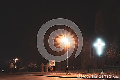 An old Victorian church with a glowing cross on a winters night Stock Photo