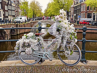 Old vintage bicycle decorated with white flowers on small bridge in old part of Amsterdam Editorial Stock Photo