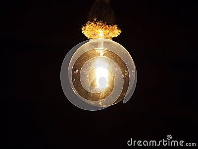 Old vintage dusty edison light bulb hanging on a rope fixture glowing against a black background Stock Photo