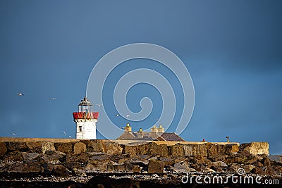 Old vintage red and white color lighthouse behind tall brown rocks. History building. Mutton island, Galway city, Ireland Stock Photo