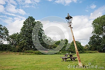 Old, vintage styled electric lamp post seen in a disused and bent position in a large beer garden. Stock Photo