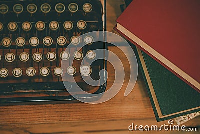 Old and vintage type writer machine and piles of books on wooden table - in vintage tone Stock Photo