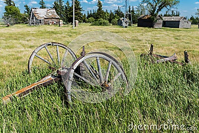 Old wagon wheels in an abandoned prairie yard with an old farmhouse, wind mill, and bins in the background Stock Photo