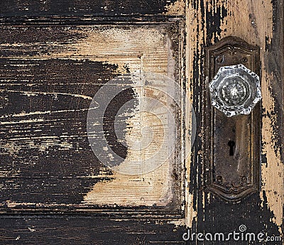 Old weathered antique beat-up wood panel door with chipped peeling paint and glass crystal doorknob and rusty plate Stock Photo
