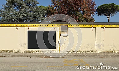 Old weathered bus stop sign on sidewalk with empty black billboard on wall behind. Asphalt road in front. Stock Photo