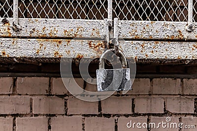 Old weathered closed gray padlock against the background of an iron box grating walls industrial background Stock Photo