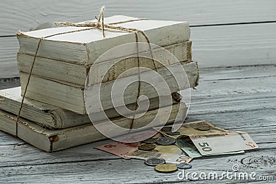 Old white books with money and coins on wooden background Stock Photo