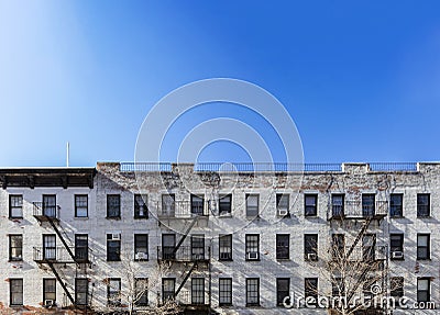 Old white brick apartment building with windows and fire escapes and an empty blue sky background overhead in New York City Stock Photo