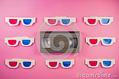 Old white paper 3d glasses with blue red lenses and black videotape on pink background. Retro video cassette with Stock Photo
