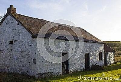 An old whitewashed stone built Irish Cottage with a small annex roofed with bangor Blue roofing tiles and rusting corrugated tin s Editorial Stock Photo