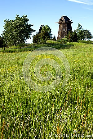 Old windmill without blades and trees next to a field Stock Photo