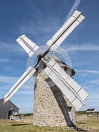 An old windmill on the coast of Normandy. Stone structure, wooden gears and bare white coated blades Stock Photo