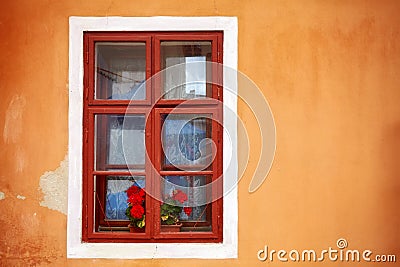 An old window with red flowers in orange wall. Stock Photo