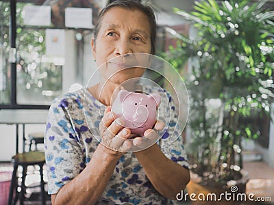 Old woman holding Pink piggy bank with two hands. Saving money for future plan and retirement fund concept Stock Photo