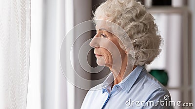 Old woman looking in window thinking lost in sad thoughts Stock Photo