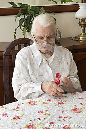 The old woman lubricates the hands creme sitting at the table. Stock Photo